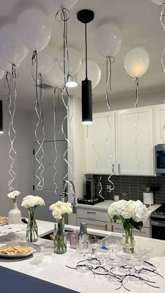 balloons are hanging from the ceiling above a kitchen counter with plates and glasses on it