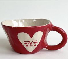 a red and white coffee cup with a face painted on the side is sitting in front of a white background