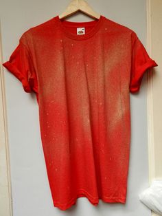 a red t - shirt hanging on a white wall next to a wooden hanger