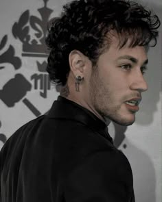 a man with black hair and piercings standing in front of a wall wearing a black shirt