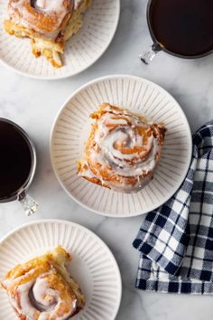 three plates with cinnamon rolls on them and two cups of coffee