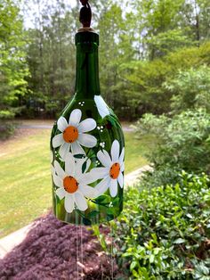 a green glass bottle with white flowers hanging from it's side in front of some bushes