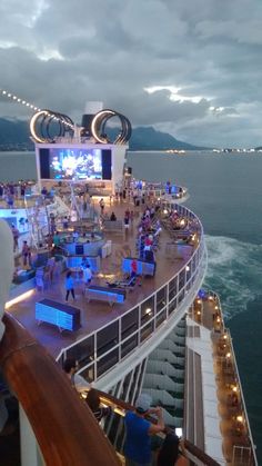 people are standing on the deck of a cruise ship at night, watching movies and dancing