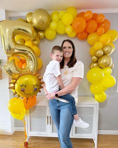 a woman holding a child in front of balloons and a sign that says 5 on it