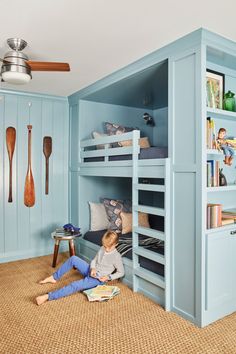 a young boy sitting on the floor in front of a bunk bed reading a book