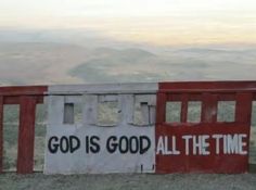 a red and white sign that says god is good all the time on top of a hill