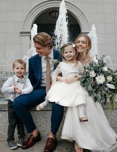 a man and two children sitting next to each other in front of a water fountain