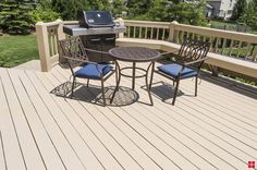 an outdoor table and chairs on a deck with bbq grill in the back ground