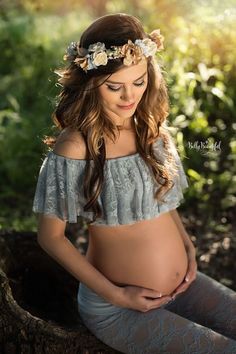 a pregnant woman is sitting in the woods with her belly exposed and flowers on her head