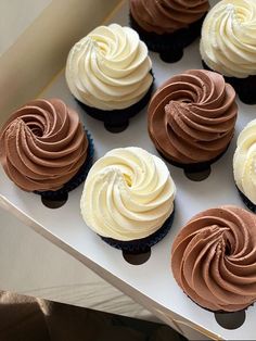 six cupcakes with white and chocolate frosting in a box on a table