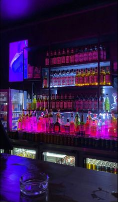 the bar is filled with bottles of alcohol and liquor glasses on the counter, as well as neon lights