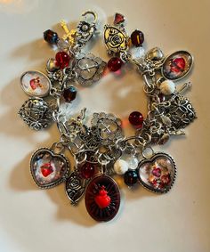 Sacred Heart Art Charms Catholic Bracelet/Semi Precious Beads. In the center is the Sacred Heart of Jesus as traditionally portrayed in many versions of artwork featuring Jesus. This resin cameo is done in red with a black antiqued finish. It is set in an antiqued silver tone vintage style bezel. This is the largest piece on the bracelet measuring 2 inches.  There are four more vintage Art Charm Sacred Heart colored images on the bracelet. Two are hearts. They are from vintage and antique prayer cards. I've downsized and set under glass and into brass bezels.  Various crosses, Milagro hearts with flowers and crown charms in both brass and silver tone. The stones and beads are  Czech Picasso beads in Mulberry  Vintage Austrian Crystals with vintage Czech Raspberry and blue beads. Natural Wh