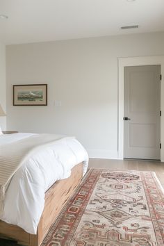 a bedroom with a bed and rug on the floor in front of a white door