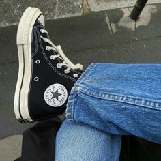 someone wearing black and white converse shoes sitting on the ground