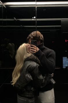 a man and woman standing in front of a mirror taking a selfie with their cell phone