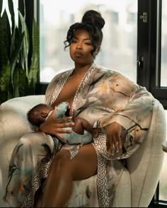 a woman sitting on a couch holding a baby in her lap and wearing a robe