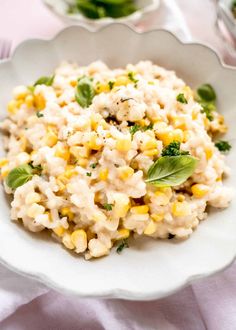 a white bowl filled with rice and corn on top of a table next to silverware