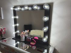 a vanity mirror with lights on top of it next to a vase filled with flowers