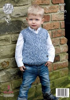 a young boy standing next to a brick wall wearing a blue vest and jeans with white shirt