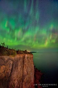 an aurora bore over the ocean with green and purple lights in the sky above it