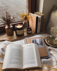 an open book sitting on top of a bed next to a candle and some books