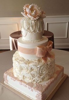 a three tiered wedding cake with flowers and pearls on the top, sitting on a table