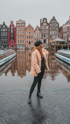 a woman standing in front of a body of water with buildings and boats behind her