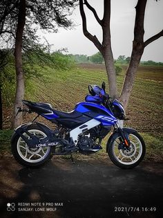 a blue motorcycle parked next to a tree in the middle of a field with leaves on it