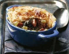 a casserole with meat and vegetables in a blue dish next to a spoon