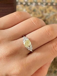 a woman's hand with a yellow and white diamond ring on top of it