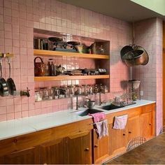 a kitchen with pink tiled walls and wooden shelves filled with pots, pans, and utensils