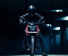 a man riding on the back of a motorcycle in a dark garage with his arms outstretched