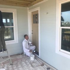 a man is painting the outside of a house while another man stands on a ladder