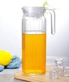 a glass pitcher filled with liquid sitting on top of a cutting board next to ice cubes