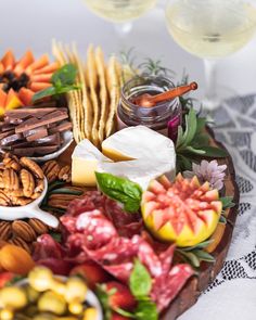 an assortment of cheeses, meats and fruit on a platter with wine glasses in the background