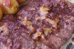 some meat and potatoes are on a plate with a flowered table cloth in the background