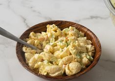 a wooden bowl filled with macaroni salad next to a jar of mayonnaise