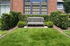 a wooden bench sitting in front of a lush green lawn next to a brick building