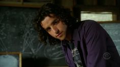 a man with curly hair wearing a purple shirt and tie in front of a chalkboard