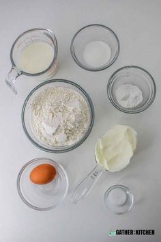 eggs, flour and butter are in bowls on a white counter top with measuring spoons