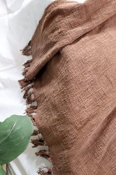 a brown blanket sitting on top of a bed next to a plant