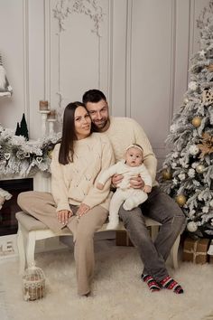 a man and woman sitting on a bench with a baby in front of a christmas tree