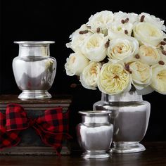 white roses are in silver vases on a wooden table next to other metal containers