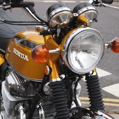 the front end of a yellow motorcycle parked on the side of the road with it's lights on