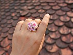 a woman's hand holding a pink flower ring on top of a red tiled roof