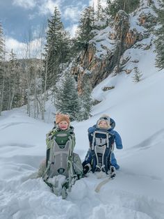 two children sitting in the snow with backpacks