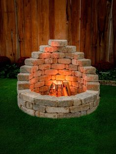 a fire pit made out of bricks in the grass with lights shining on it's sides