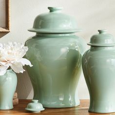 three green vases sitting on top of a wooden table next to a white flower