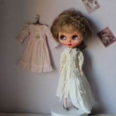 a doll is standing on a pedestal next to a wall with pictures and clothes hanging above it