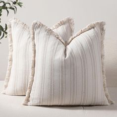 two white pillows sitting on top of a couch next to a potted green plant